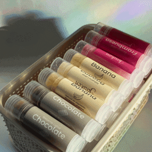 Tubos de balsamo labial de color gris, amarillo y rojo dentro de una canasta de mimbre